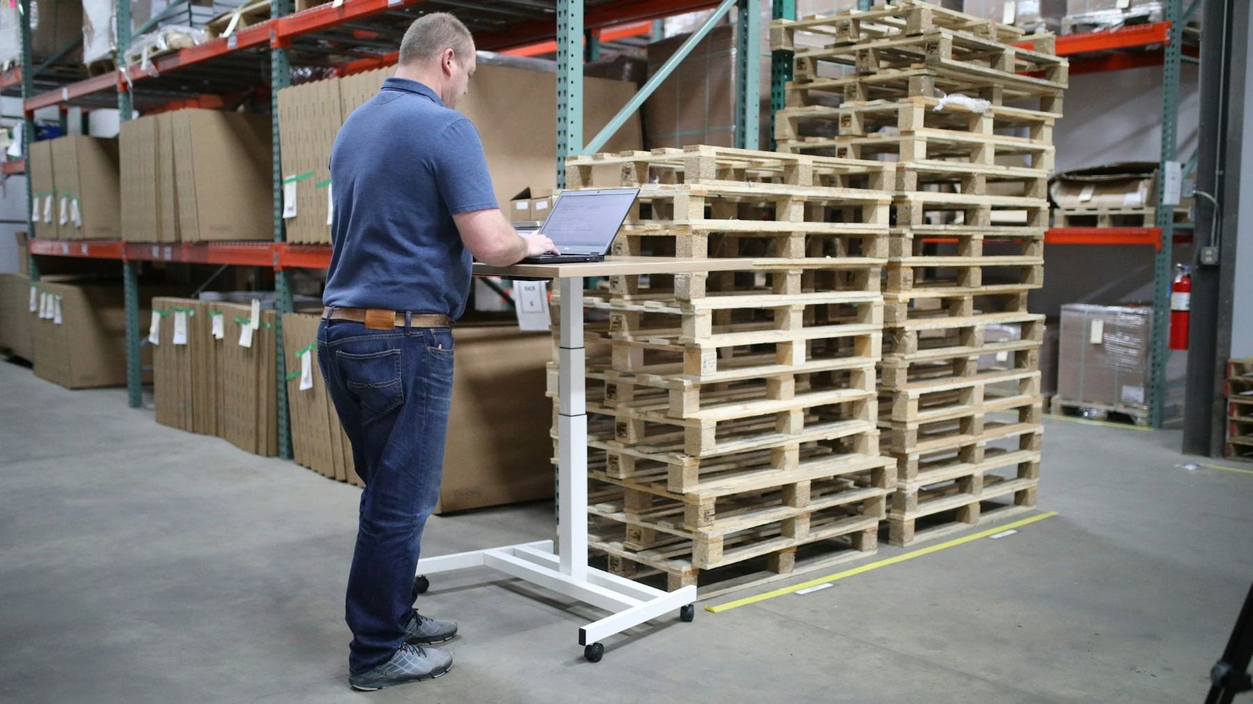 Lagermedarbeider med laptop mellom paller og reoler – grossist